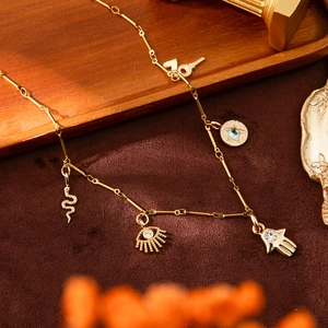 Gold Hamsa and snake charm necklace with blue crystal accents in bohemian design