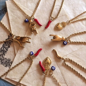 Detailed close-up of gold Mano Cornuta, evil eye, and Cornetto pendants on twist chains