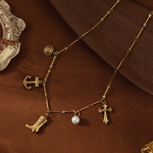 Collier vintage doré avec pendentifs ancre, croix et botte sur un fond texturé élégant