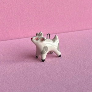 Detailed macro view of a handmade ceramic goat pendant with grey spots on pink background