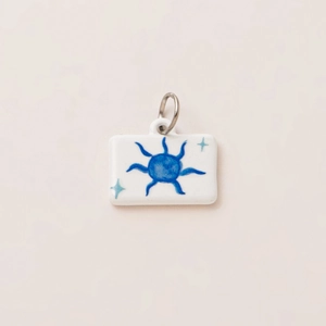 Detail view of rectangular white pendant with blue sun and green star motifs