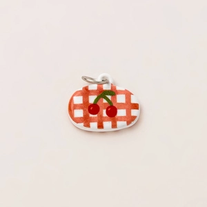 Macro view of oval cherry pendant with red checkered pattern and 18K gold plated ring
