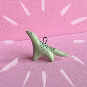 Macro view of light green enamel dinosaur pendant with metal ring on pink background
