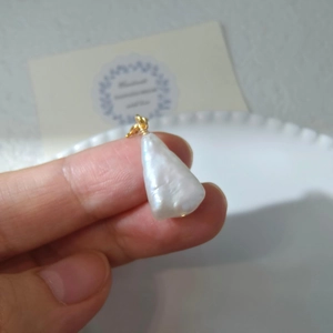Macro detail of large baroque pearl pendant with gold wire wrap held by a hand