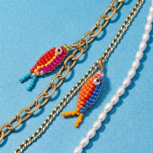 Makro-Detail von bunten Perlenfisch-Anhängern an Goldketten und weißen Perlenketten