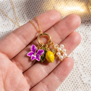 Collier doré 18K avec breloques citron, fleur violette, feuille verte et perles en main