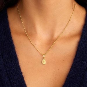 Makroaufnahme der goldenen Kugelkette mit ovalem Relieff-Anhänger auf blauem Pullover