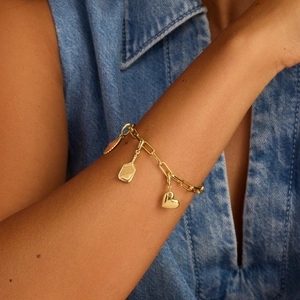 Nahaufnahme eines goldfarbenen Herz-Charm-Armbands getragen zu einem Jeans-Outfit