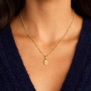 Detailansicht einer goldenen Volleyball-Halskette auf einem blauen Strickpullover