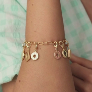 Dettaglio del bracciale dorato con ciondoli colorati a forma di ciambella e macaron al polso