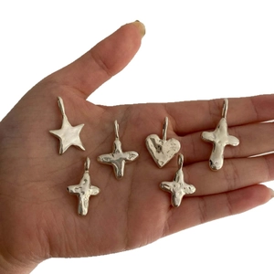 Lava texture silver pendants featuring heart, star, and cross shapes on a palm