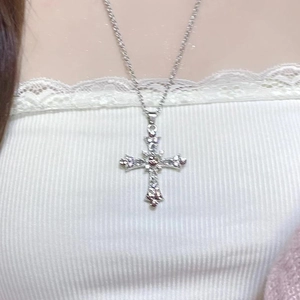Close-up of gothic cross necklace with pink zircons worn on a white textured top