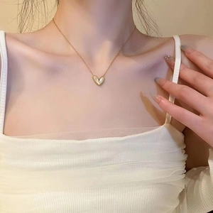 Detail of elegant gold heart necklace with white pearl inlay worn by a model