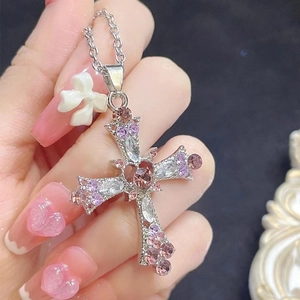 Macro detail of gothic cross pendant featuring pink heart gemstone and rhinestone accents