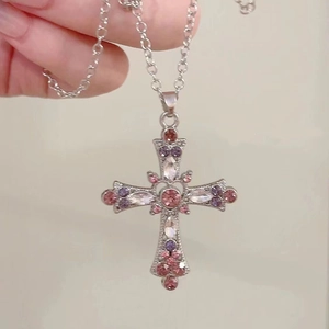 Gothic Y2K silver cross necklace with pink and purple rhinestones held by a hand