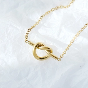 Collier minimaliste avec pendentif nœud doré et chaîne fine sur fond blanc texturé