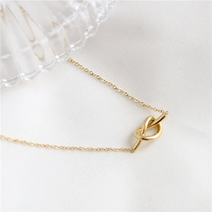 Collier minimaliste en or avec pendentif à nœud et chaîne fine sur fond blanc épuré
