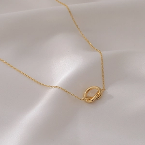 Vue détaillée du collier pendentif nœud doré minimaliste sur un tissu en soie blanc