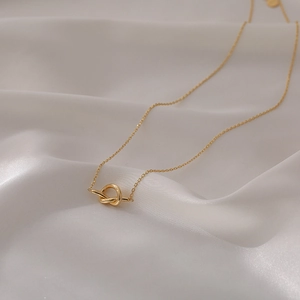 Collier minimaliste avec pendentif nœud doré et chaîne fine sur tissu en soie blanche