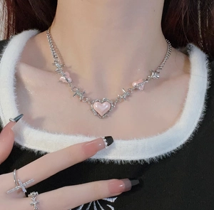 Detail view of Y2K style silver necklace with pink hearts and a cross ring on model