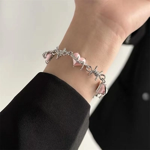 Detail of pink heart accents on silver-toned thorn chain bracelet worn on wrist