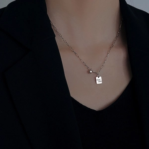 Detalle del collar plateado con colgante cuadrado Good Luck sobre un traje negro formal