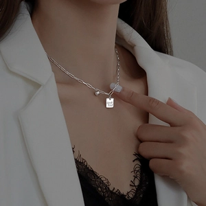 Detalle de collar plateado con colgante Good Luck y perla usado por una modelo