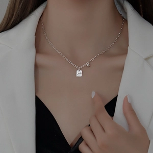 Detalle de collar de cadena de clip plateado con colgante rectangular y cuenta al cuello