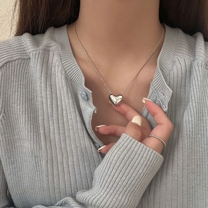 Polished silver heart pendant necklace on model wearing a light blue knit sweater