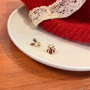 Close-up of reindeer and red gift box Christmas stud earrings on a white ceramic plate