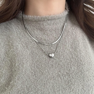 Detail of silver heart pendant and layered snake chain on grey knit sweater