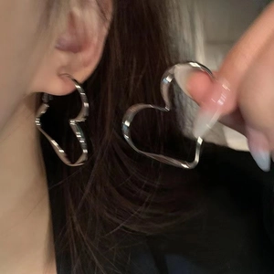 Detail shot of large silver twisted heart hoop earrings in a minimalist metallic finish