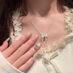 Detalle del collar con colgante de lazo plateado y acabado metálico mate sobre encaje