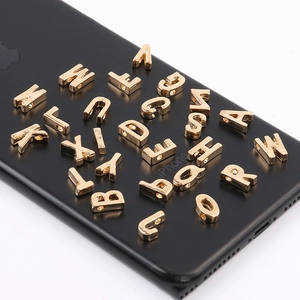 Dettaglio macro di ciondoli lettere 3D in lega dorata con fori per gioielli fai-da-te