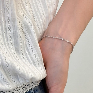 Pulsera de cadena de plata minimalista con diseño trenzado en la muñeca de una mujer