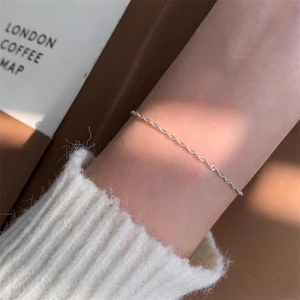Detalle de una pulsera minimalista de cordón plateado en la muñeca de una mujer