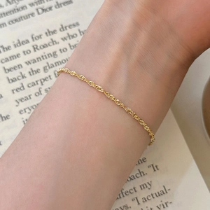Primer plano de una pulsera minimalista de cadena de cuerda torcida dorada en la muñeca