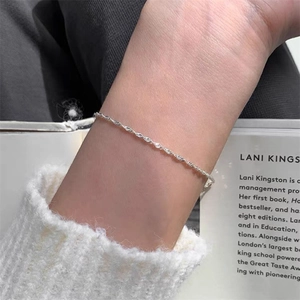 Primer plano de una pulsera minimalista plateada de cadena trenzada en la muñeca