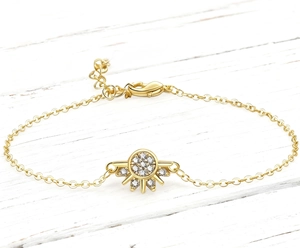 Dettaglio di un bracciale dorato con ciondolo a sole, pietre di zircone e chiusura a moschettone