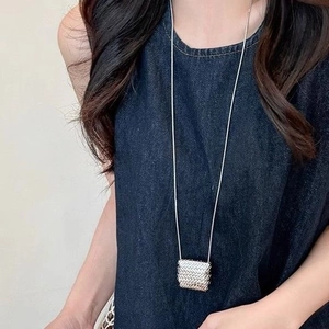 Close-up of a long necklace with a woven texture square pendant worn on a denim outfit