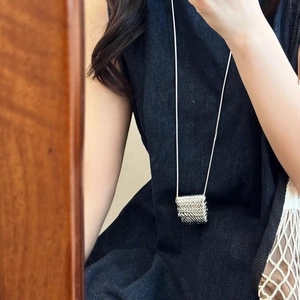 Modern silver rectangular necklace with woven texture on long chain worn on denim