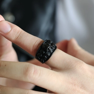 Macro close-up of a wide black stainless steel ring with embossed skulls in punk style