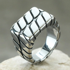 Makroansicht eines Herrenrings aus Edelstahl mit geometrischer Textur auf einem Stein