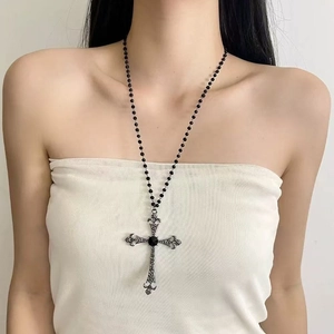 Détail d'un pendentif croix gothique avec gemme noire sur un collier punk style Y2K
