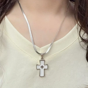 Close-up of a silver blade chain necklace with a white enamel cross pendant on a model