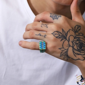 Nahaufnahme eines regenbogenfarbenen Edelstahlrings mit Textur auf einer tätowierten Hand