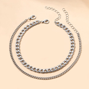 Detail of layered silver alloy anklets featuring a bold Cuban link and slim curb chain