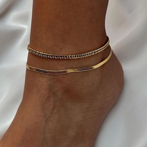 Detail of layered gold ankle chains featuring curb and herringbone styles on ankle