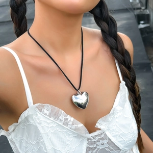Close-up of polished silver heart pendant on a black cord necklace worn by a model