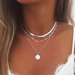 Close-up of three-layered silver necklace with snake chain and round embossed pendant